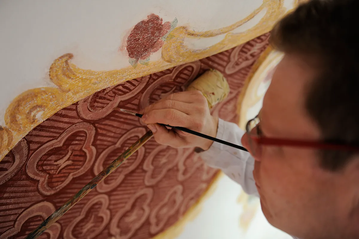 Maler- und Lackierermeister Rupert Hafner zieht feine Pinselstriche am Deckengemälde einer Kapelle.